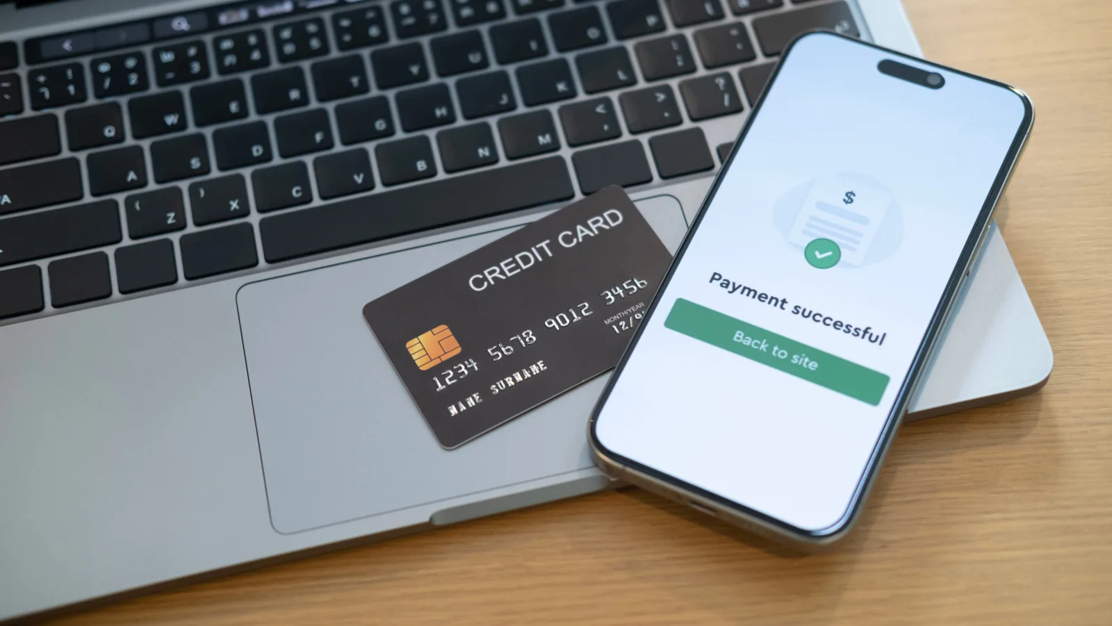 Digital payment confirmation on a mobile phone beside a card and laptop for automated supplier payouts.